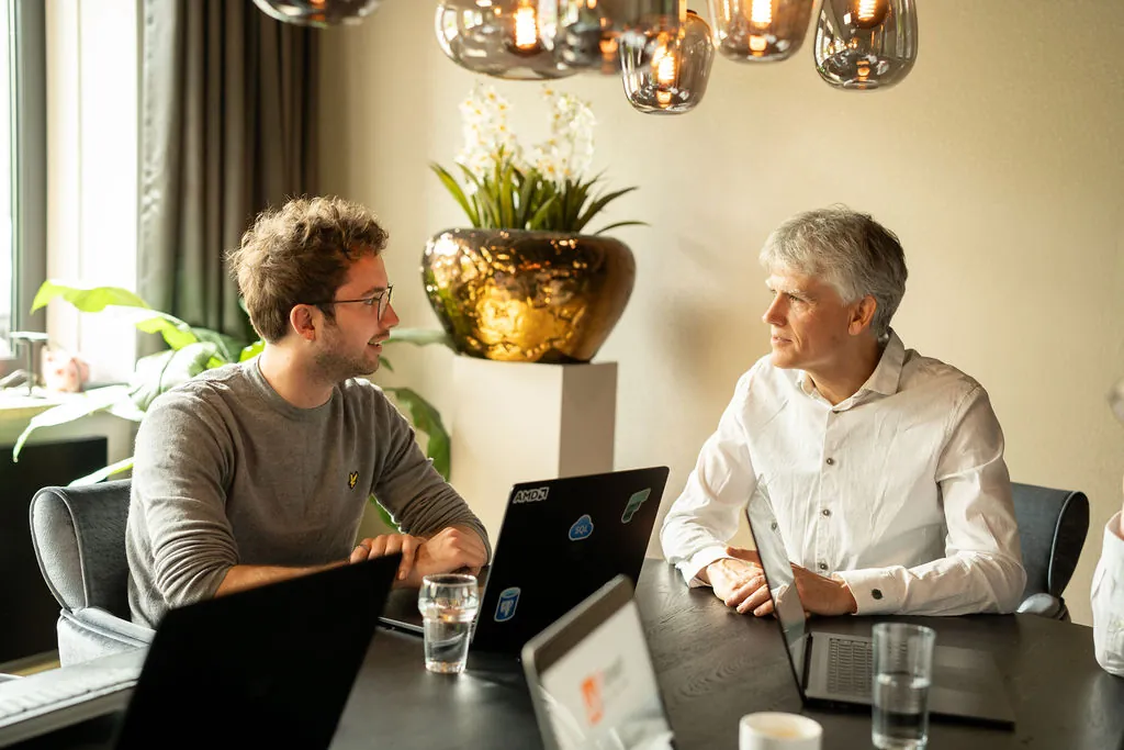 Twee collega's aan tafel met laptops, met Azure-stickers en een oranje notitieboek
