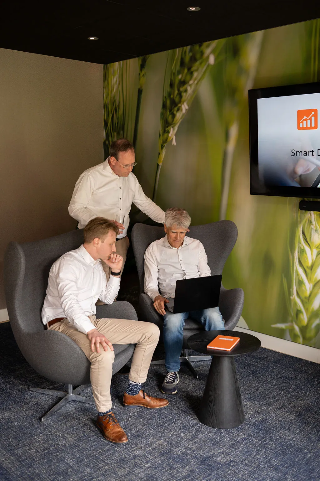 Overleg in de lounge van ITsmart, met een tv-scherm en een oranje notitieboek