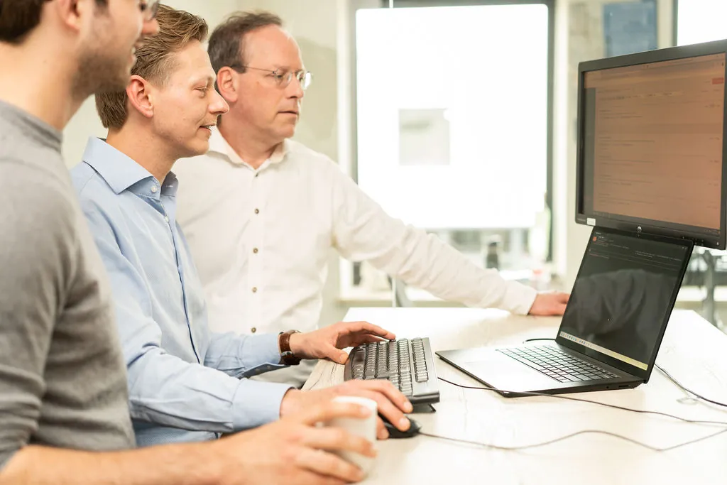 Drie collega's van ITsmart lachen bij een grote monitor in de werkruimte
